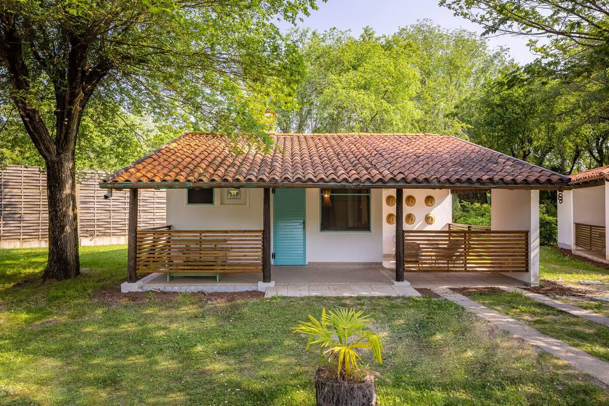 A small, single-story building with a tiled roof, a blue door, and a covered porch with benches.