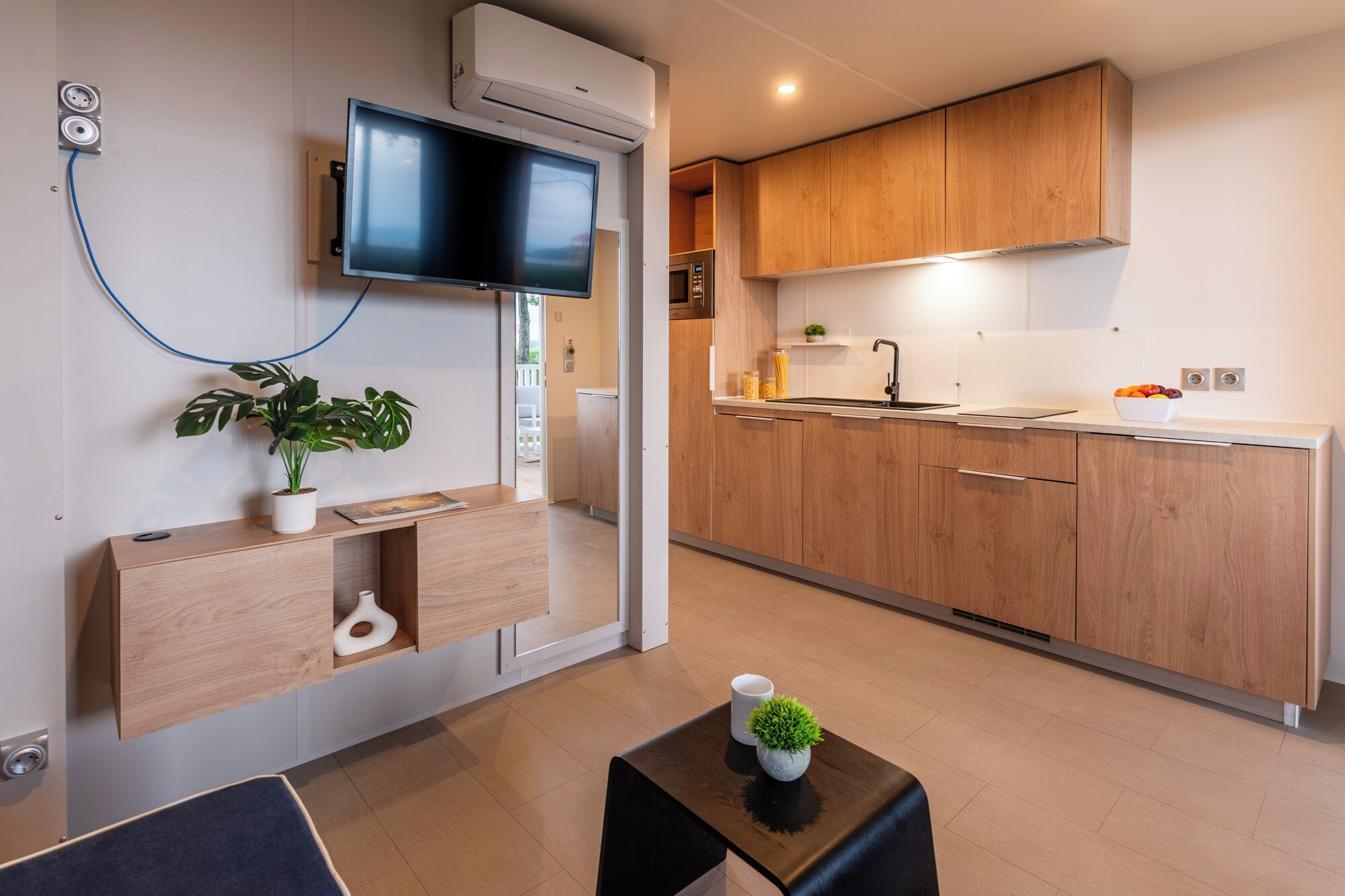 A modern kitchen with wooden cabinets, a built-in oven, and a flat-screen TV mounted on the wall.