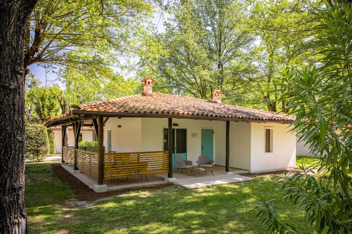 Ein kleines, eingeschossiges Haus mit einem Ziegeldach, einer Veranda mit Sitzgelegenheiten und einer Tür, die mit der Nummer 307 gekennzeichnet ist.