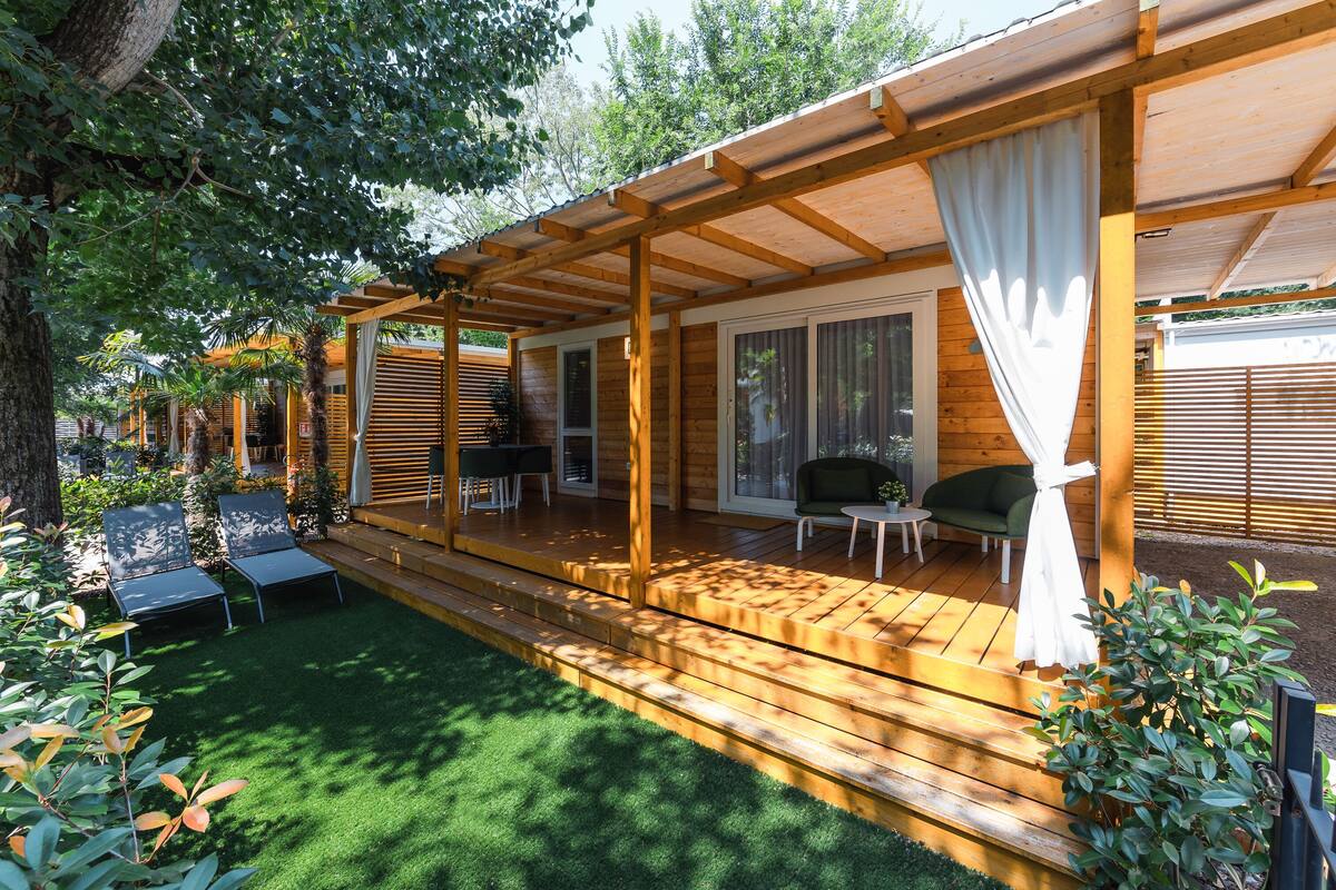 A wooden deck with outdoor furniture, a covered seating area, and a lawn.