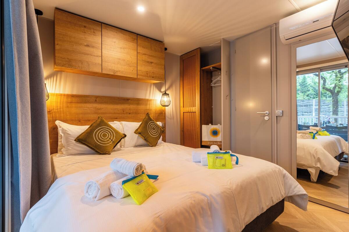 Ein Hotelzimmer mit einem Holzkopfteil, einem Bett mit weißer Bettwäsche, einem gelben Handtuch und einer sichtbaren Badezimmertür.