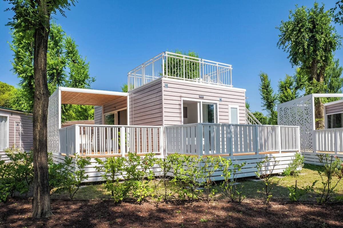 Ein modernes, mehrgeschossiges Mobilheim mit Balkon, umgeben von Bäumen und einem angelegten Garten.