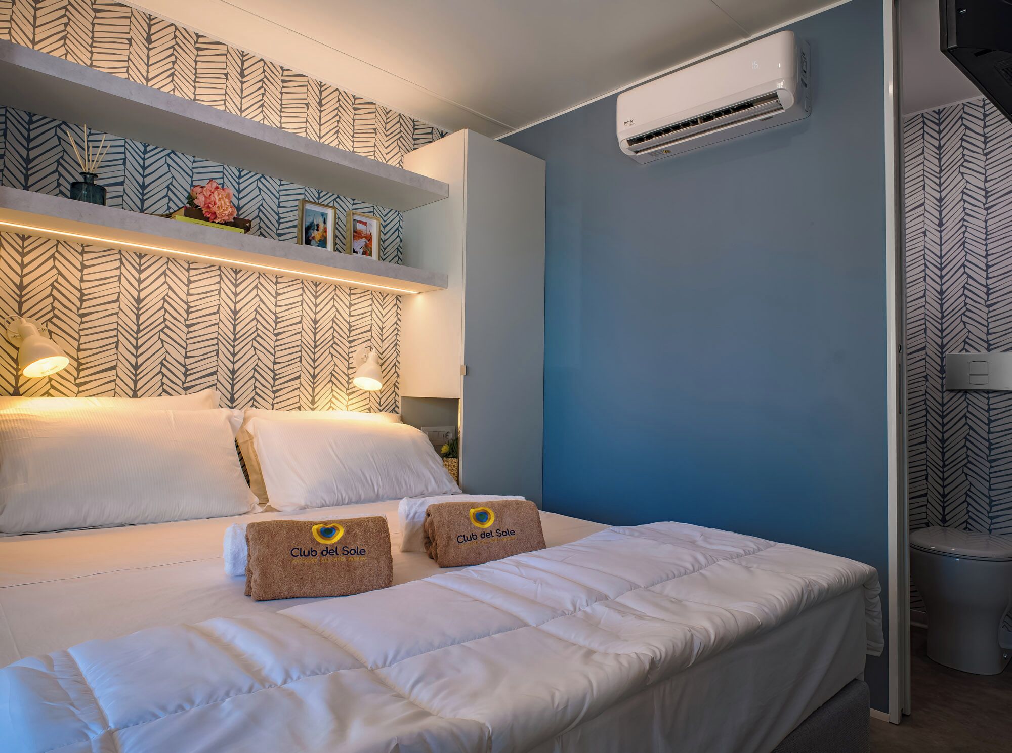Une chambre d’hôtel avec un lit, une table de chevet, un climatiseur fixé au mur et un papier peint à motifs.
