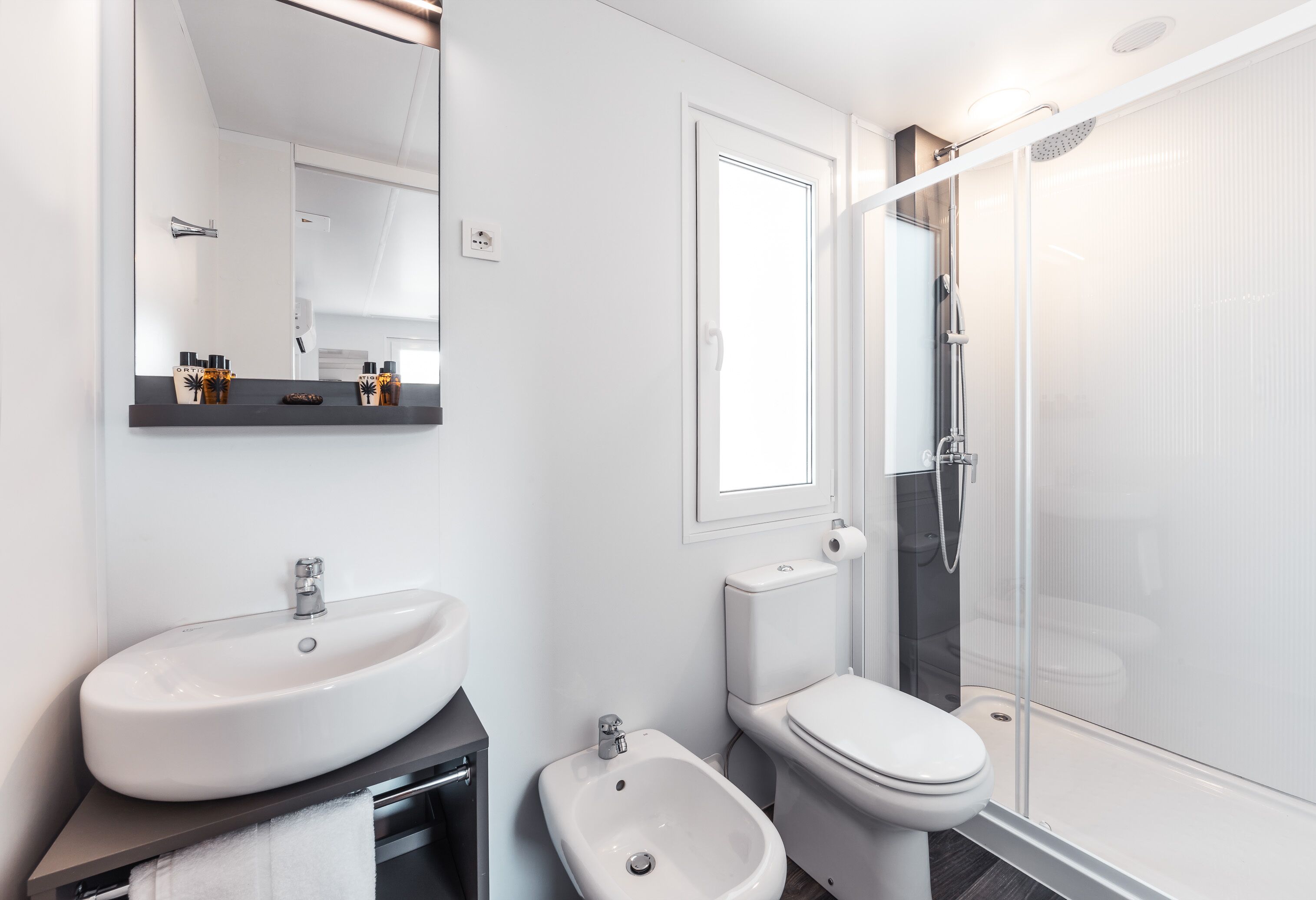 Un bagno moderno con lavandino, water e bidet bianchi, uno specchio grande e una cabina doccia in vetro.