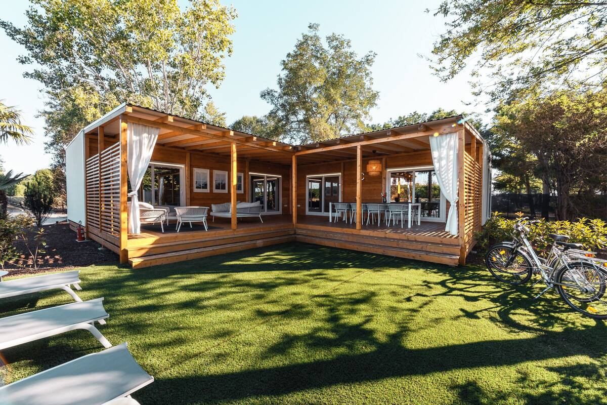 A wooden cabin with a covered patio, outdoor seating, and bicycles.