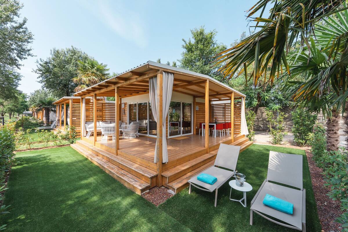 A wooden deck with outdoor furniture, a covered patio area, and a lush garden.