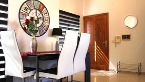 Uma sala de jantar com mesa, cadeiras, um vaso com flores, um relógio e uma porta.