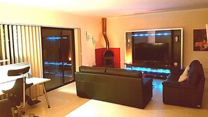 Uma sala de estar moderna com um sofá, uma poltrona, uma televisão e uma lareira.