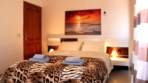 Quarto com uma cama, uma pintura de um pôr do sol sobre o oceano e uma porta de madeira.