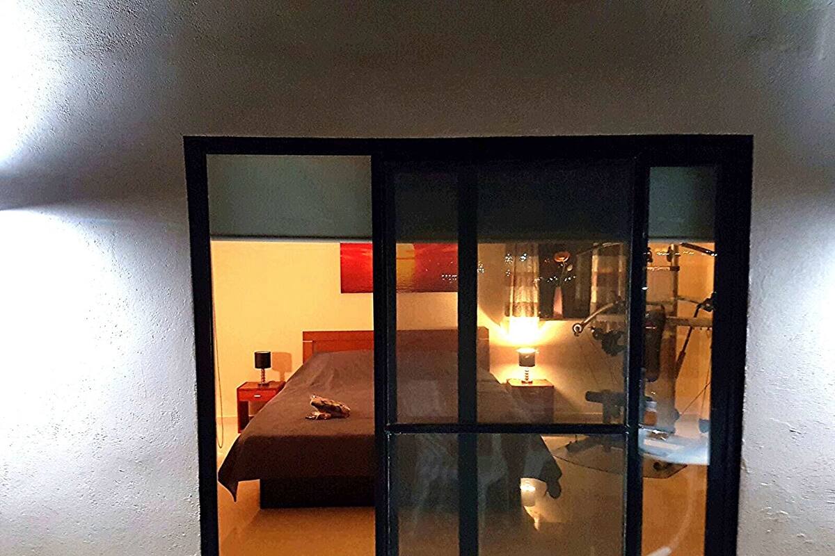 A room with a bed, a table with a lamp, and a chair.
