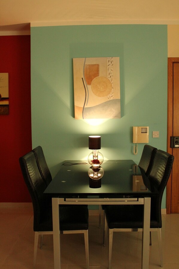 Un comedor con una mesa y cuatro sillas, un teléfono de pared y un cuadro sobre la mesa.