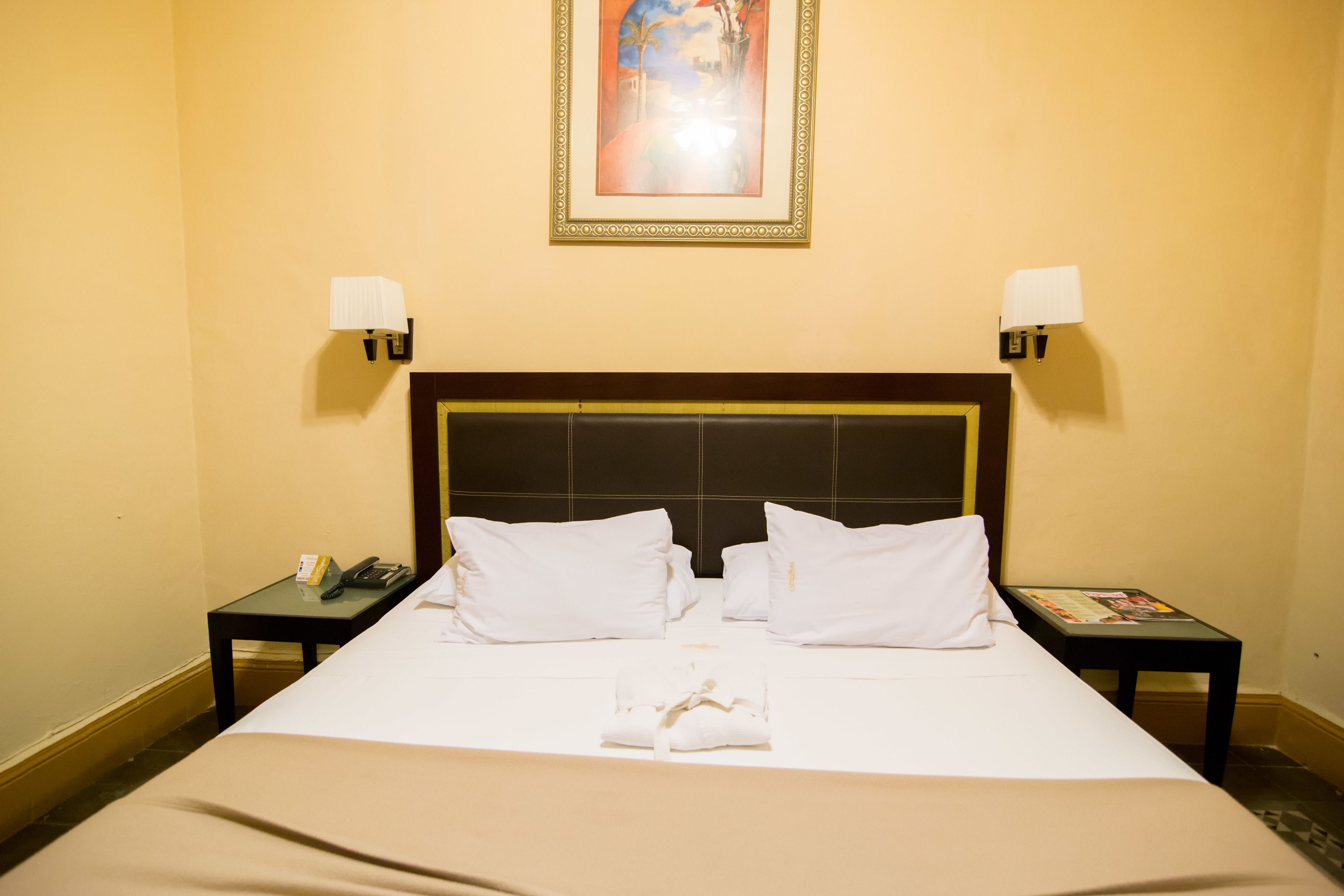 A hotel room with a large bed, two bedside tables, a nightstand, a framed picture on the wall, and a lamp on each bedside table.