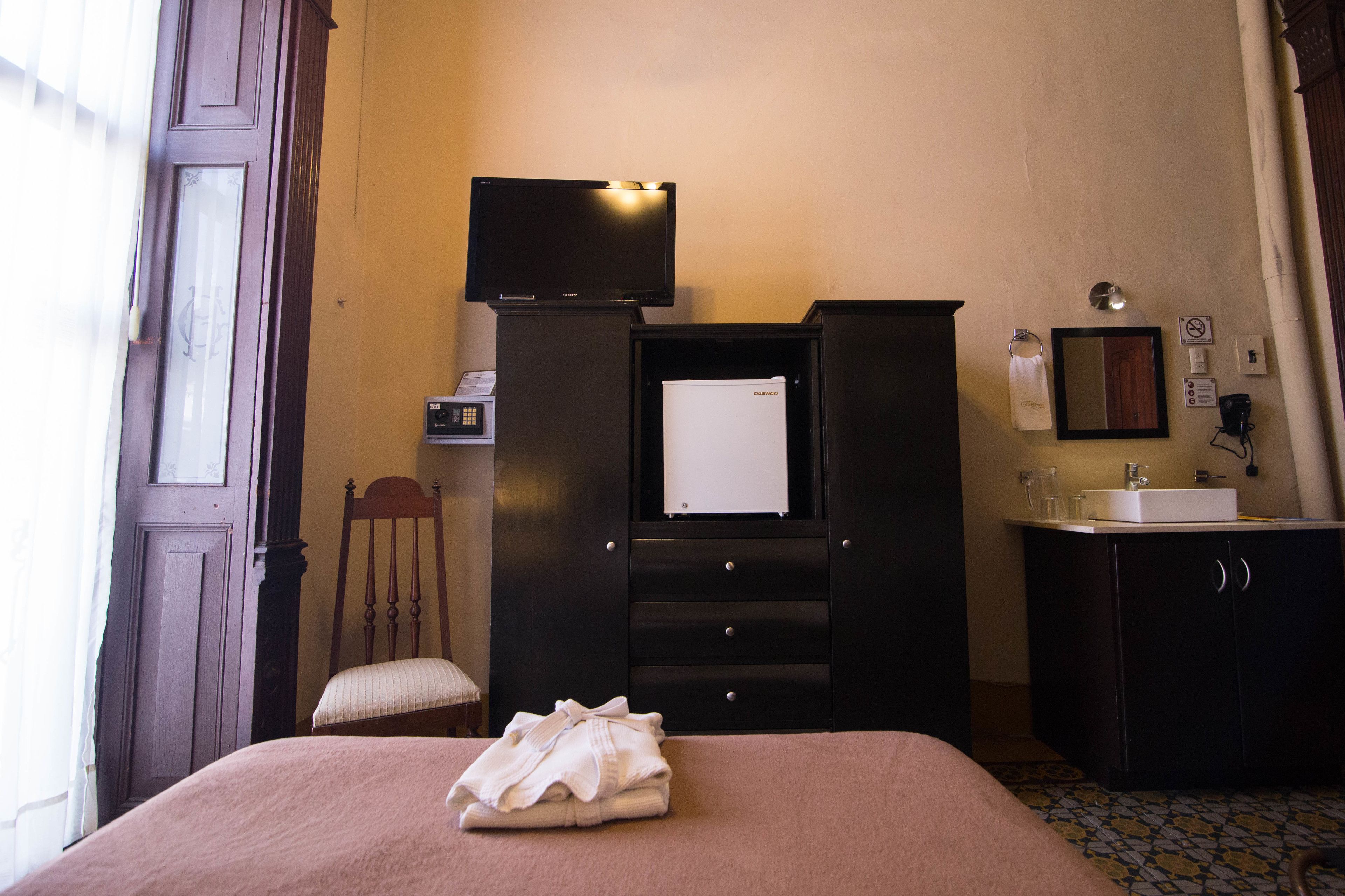 A hotel room with a bed, a television, a desk with a computer, a chair, a cabinet, and a bathroom with a sink and mirror.