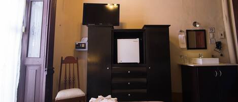 A hotel room with a bed, a television, a desk with a computer, a chair, a cabinet, and a bathroom with a sink and mirror.