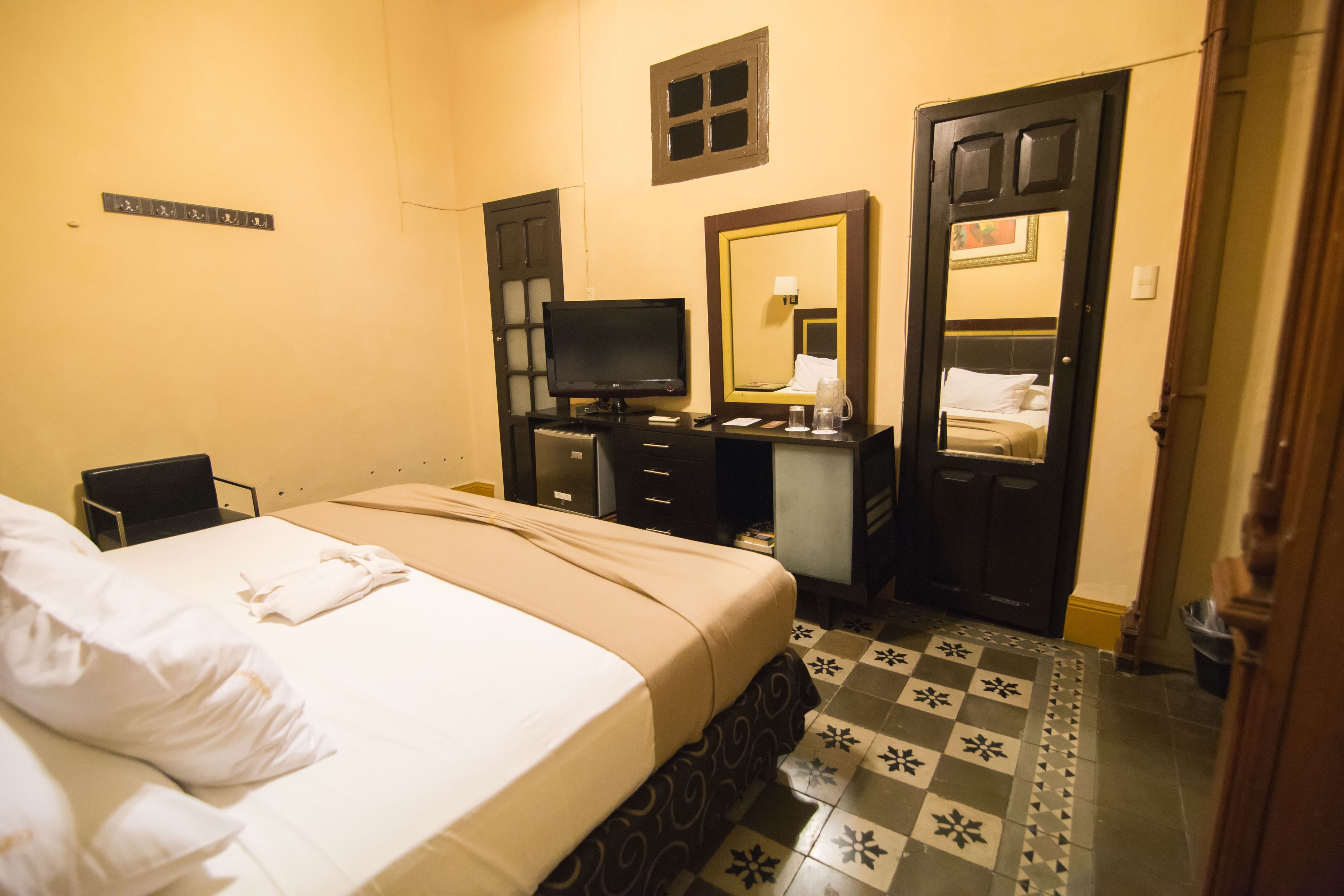 A hotel room with a bed, a desk, a television, a mirror, and a door.