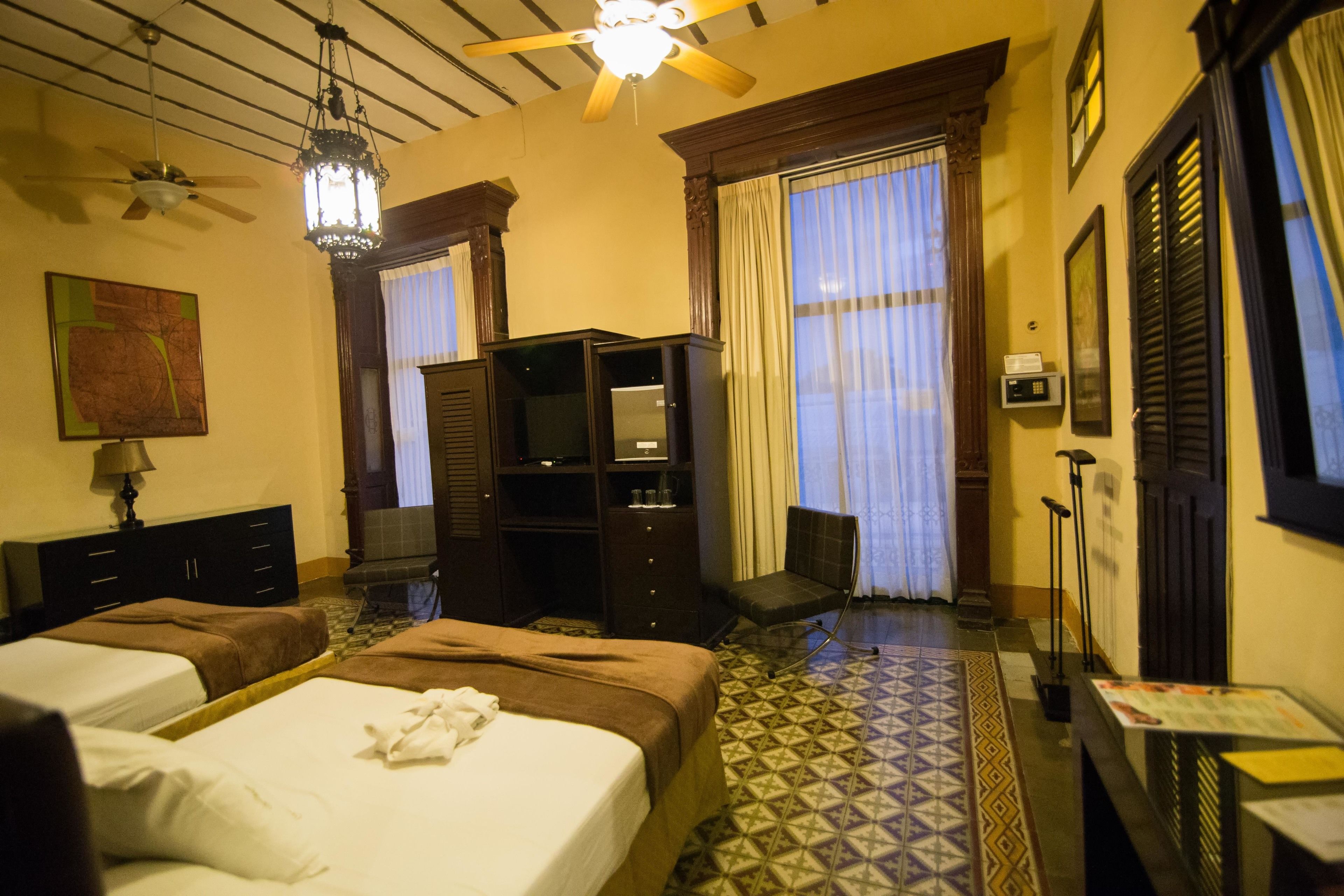 A hotel room with two beds, a ceiling fan, a television, and a small seating area.