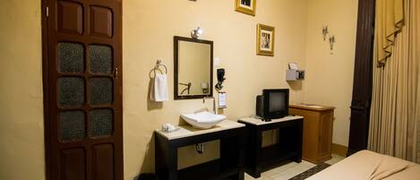 A hotel room with a wooden door, a large mirror, a sink, a television, and a bed.