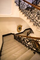 Eine Treppe mit aufwendiger schwarzer Eisenbalustrade und einem spiegelnden, goldfarbenen Rahmen.