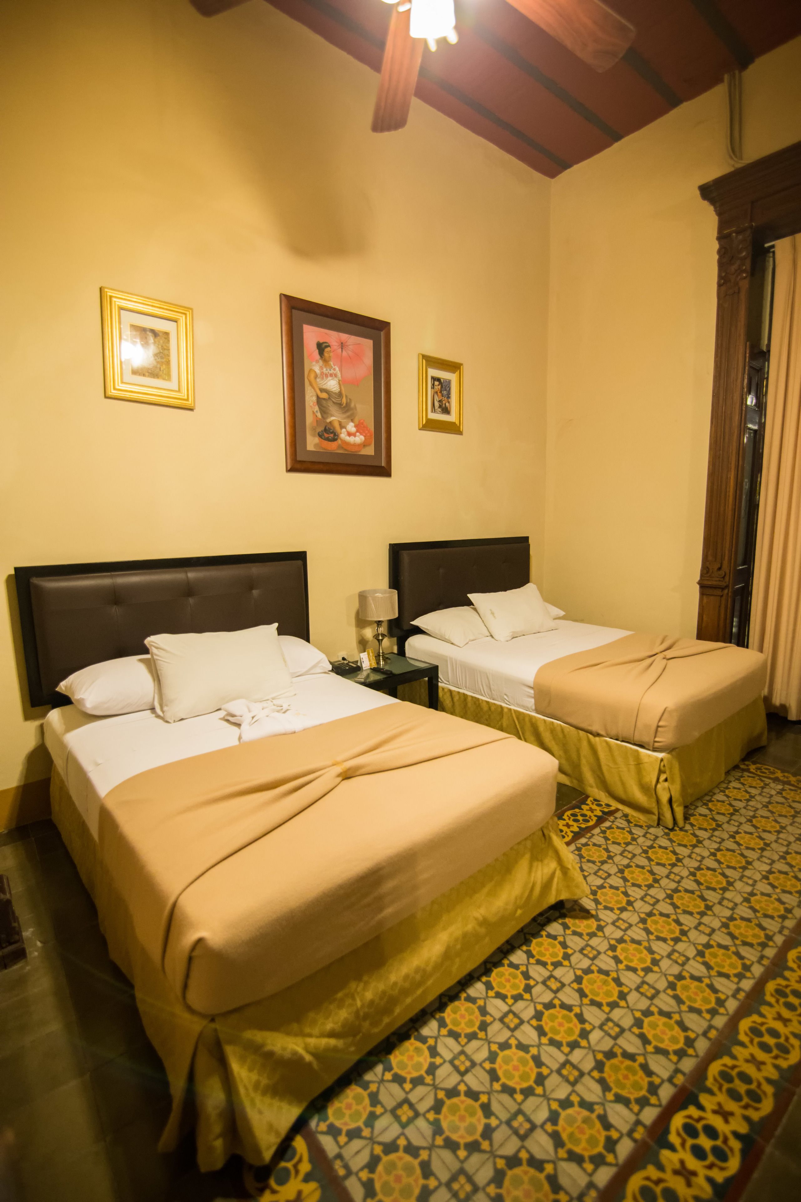 Habitación de hotel con dos camas, piso estampado y cuadros en la pared.