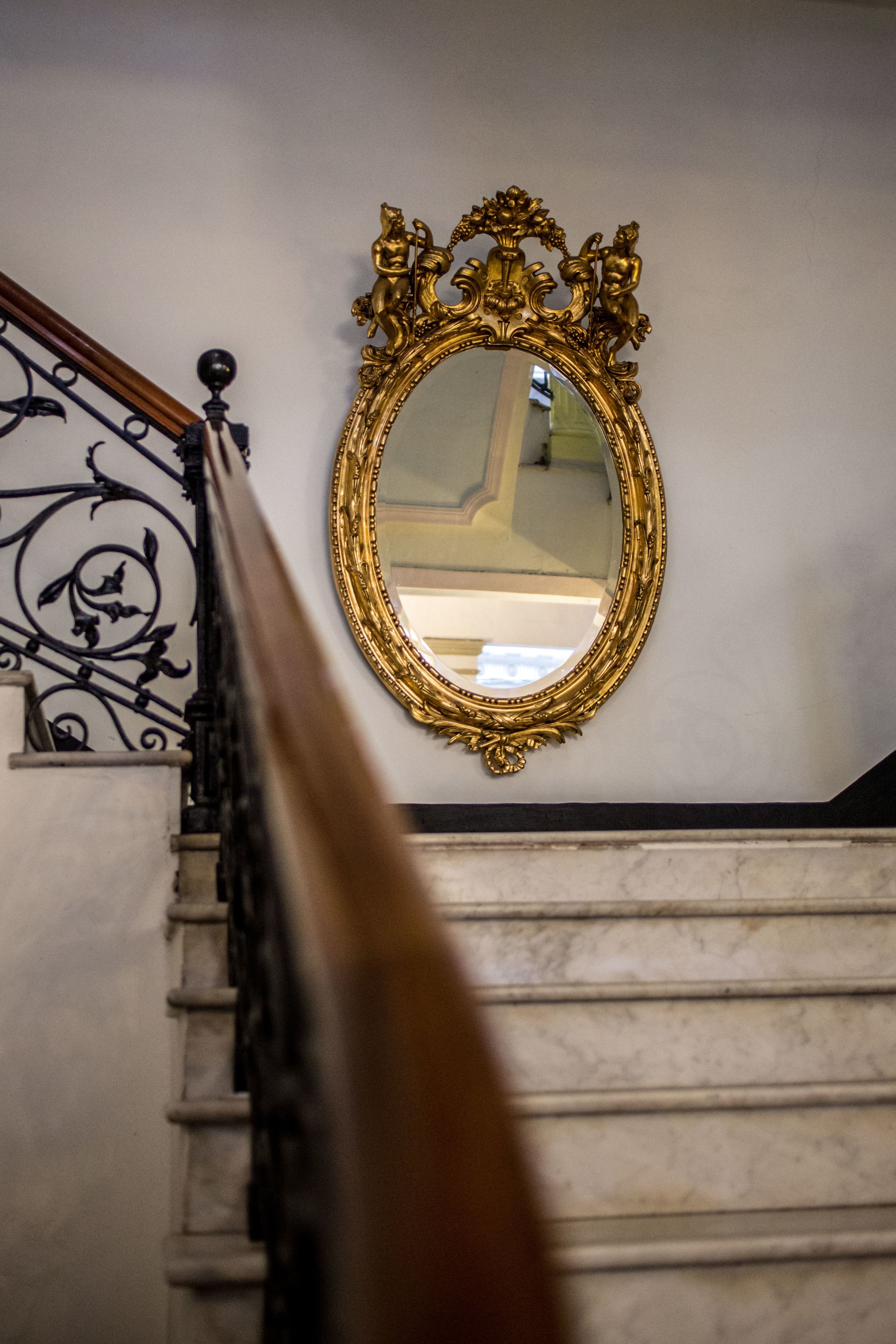 A staircase with a golden ornate mirror on the wall.