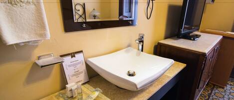 A bathroom with a white sink, a mirror, a clock, and a television.