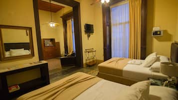 Une chambre d’hôtel avec deux lits, un bureau, un miroir, un ventilateur de plafond et une télévision.