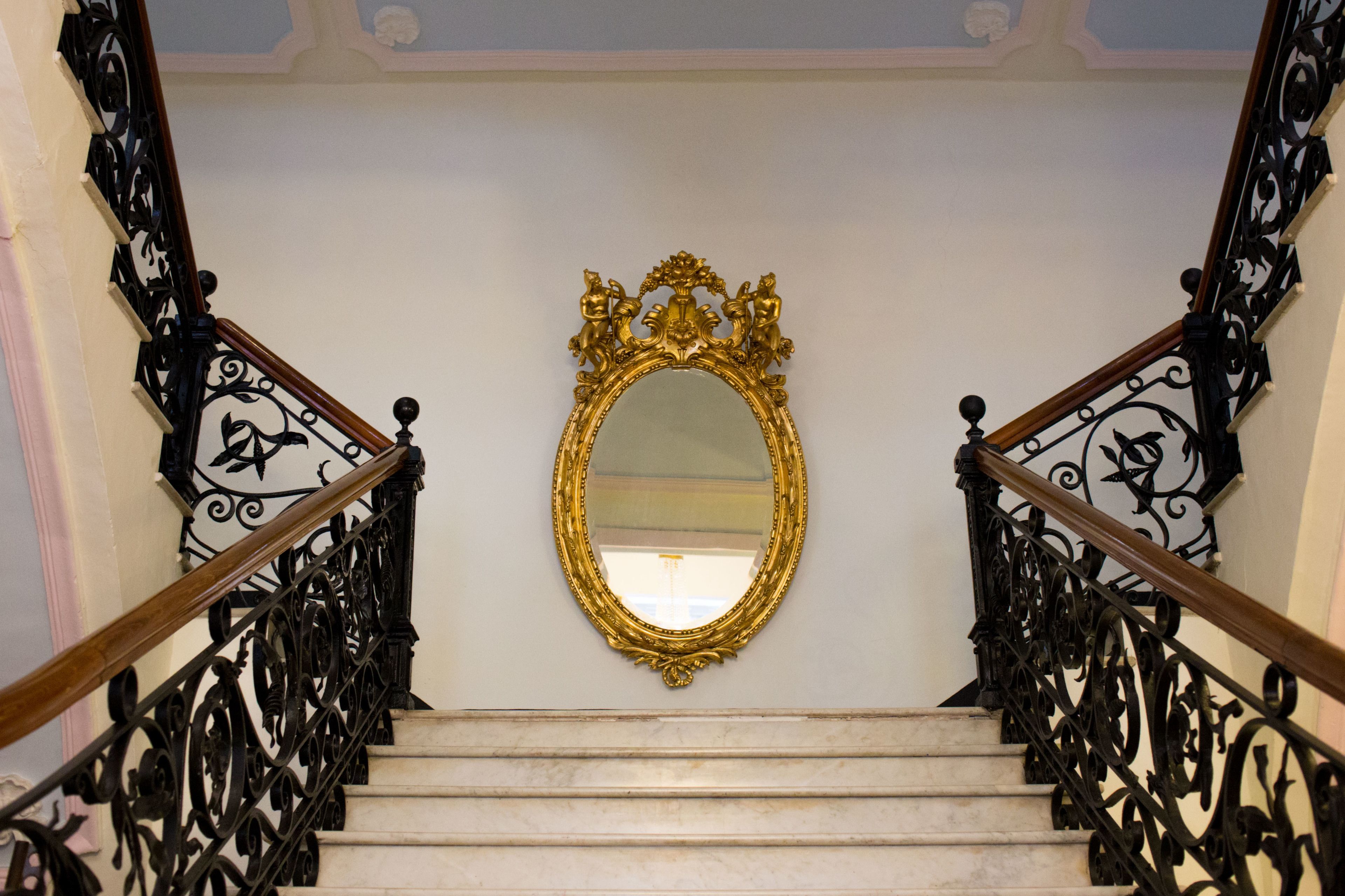 A grand staircase with ornate black railings and a gold-framed mirror above the steps.