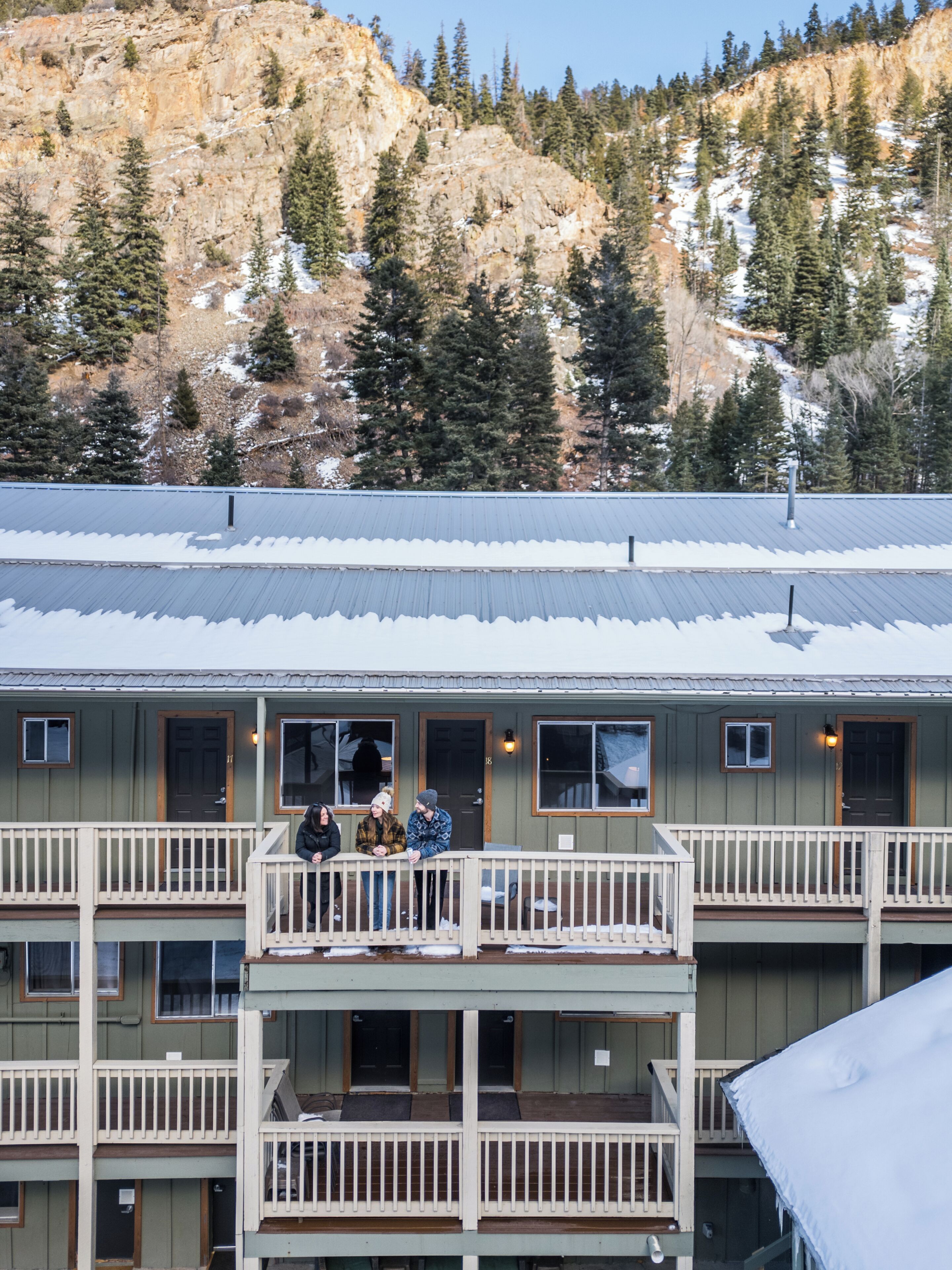A multi-story building with balconies, a metal roof, and a mountainous backdrop.