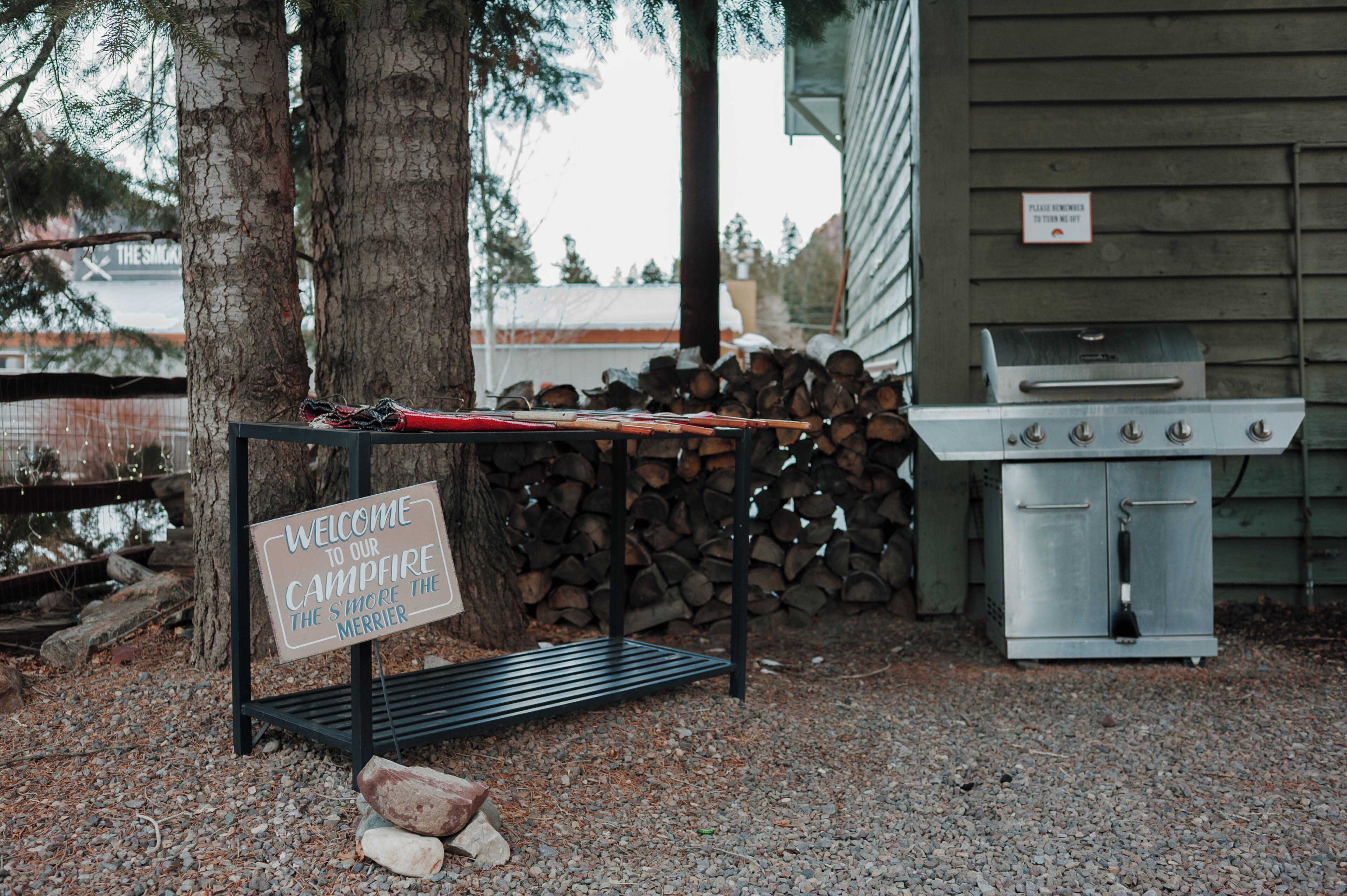 A campfire sign, a grill, and a stack of firewood.