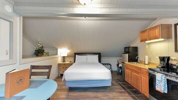 A compact room with a bed, a small table, a kitchenette, and a ceiling light.