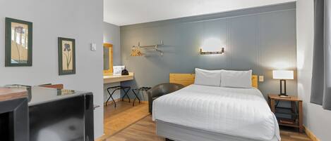 Hotellihuone, jossa on sänky, työpöytä tuolilla, televisio ja seinään kiinnitetty valaisin.