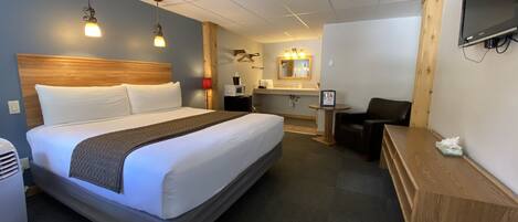 A hotel room with a large bed, a desk, a chair, a TV, a microwave, and a small table with a tissue box.