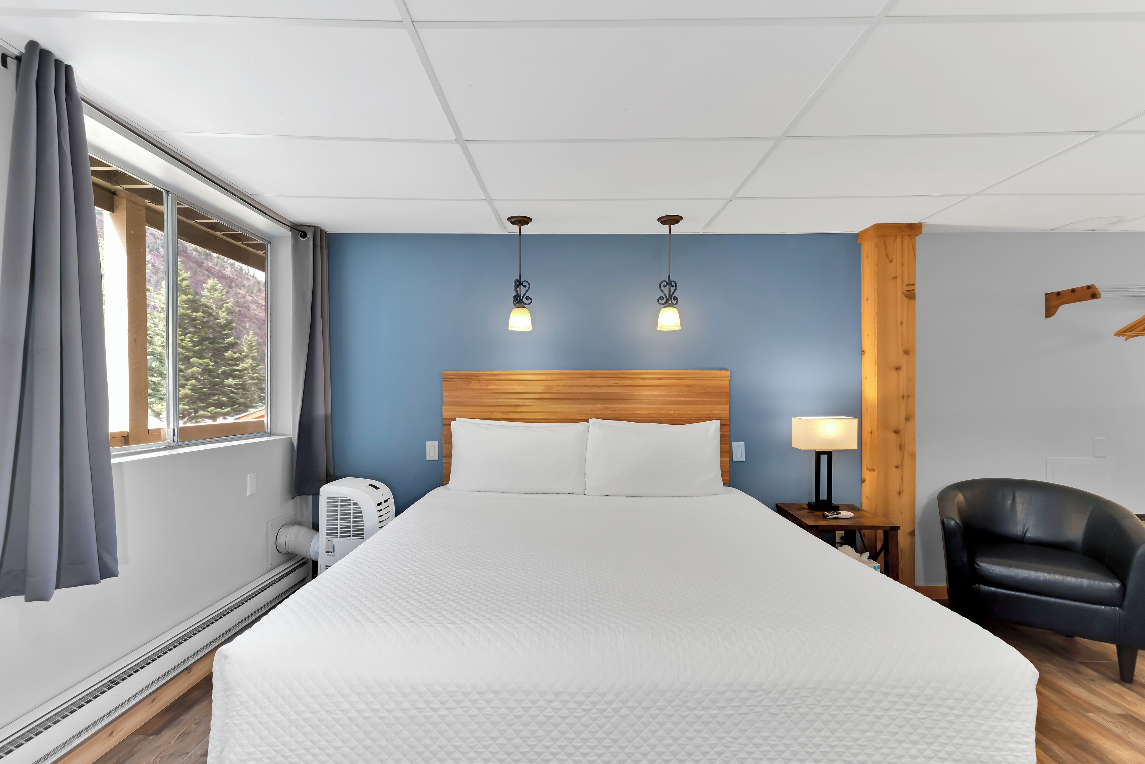 A hotel room with a large bed, a wooden headboard, a desk with a lamp, a chair, and a window with curtains.