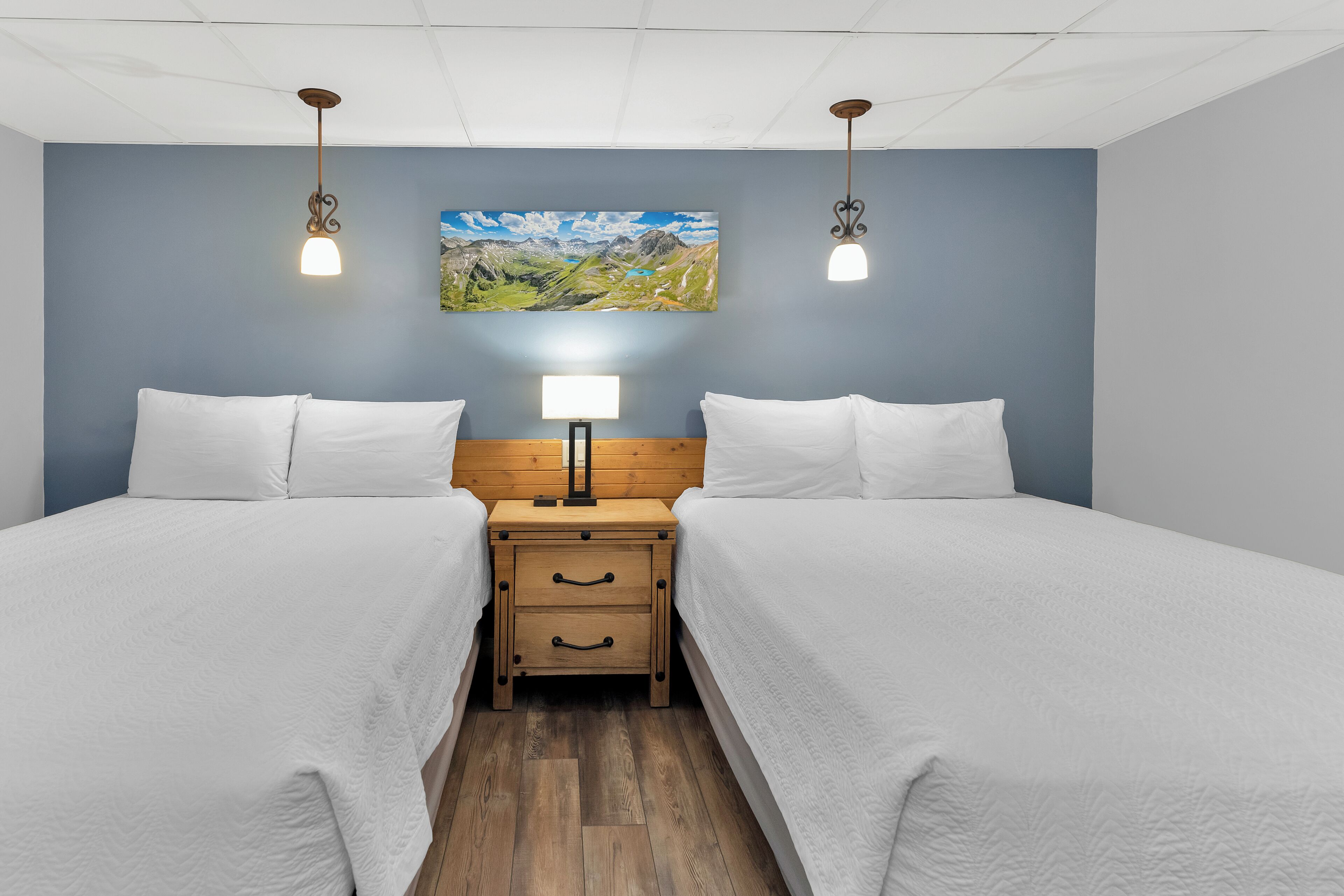 A double room with two beds, a nightstand with a lamp, and a painting on the wall.
