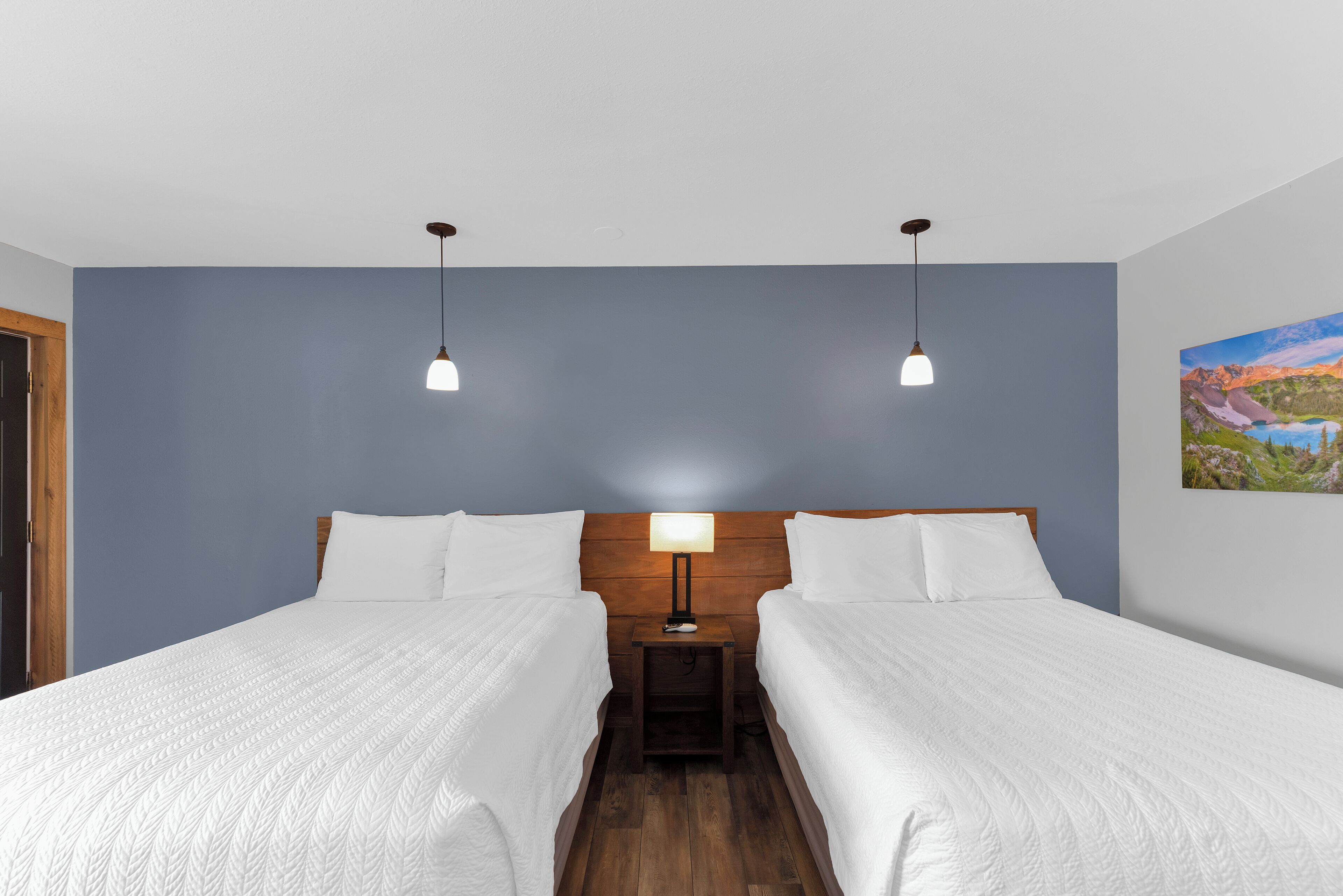 Een hotelkamer met twee bedden, een nachtkastje, een lamp en een schilderij aan de muur.