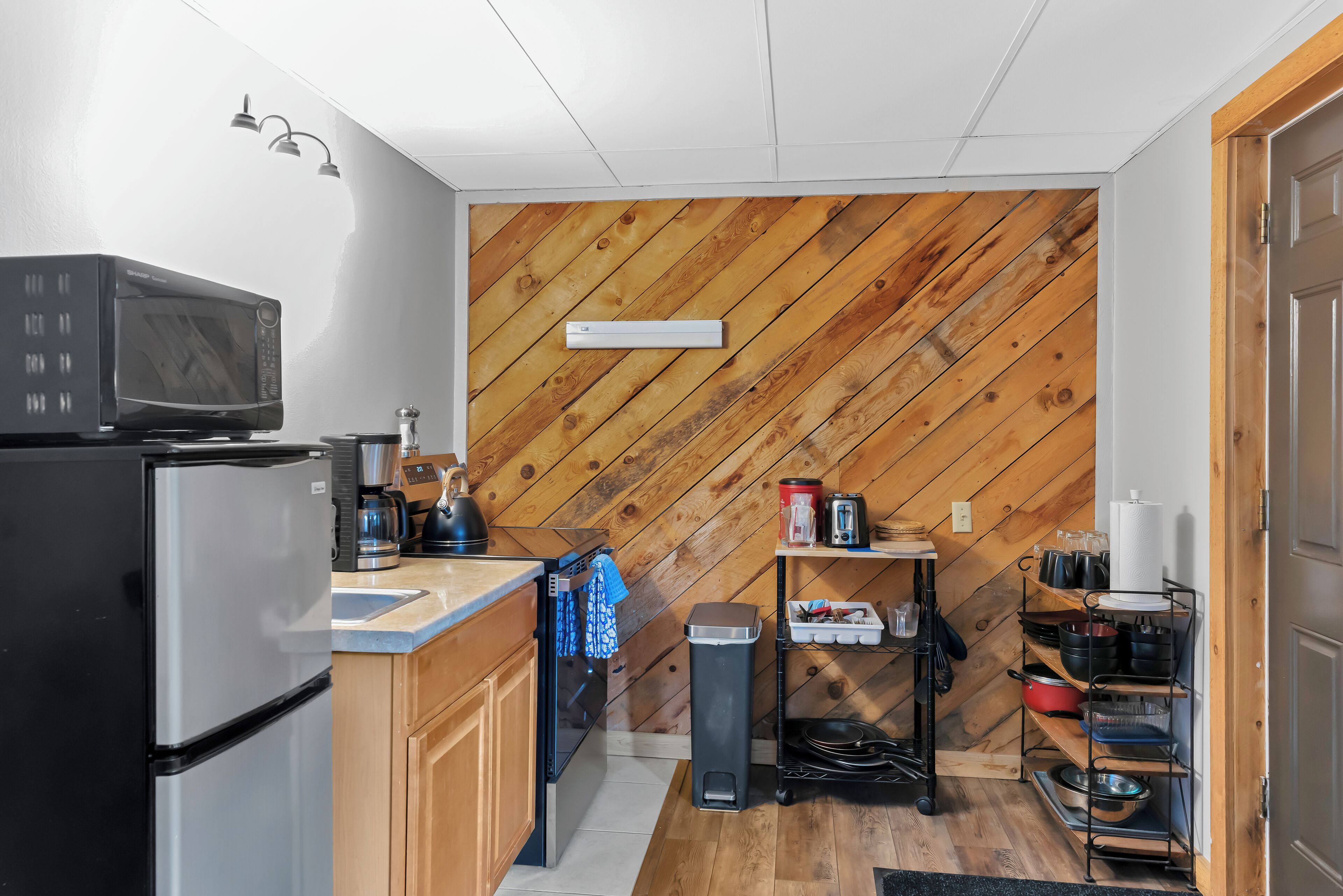 A compact kitchen with a microwave, refrigerator, coffee maker, and a wooden wall.