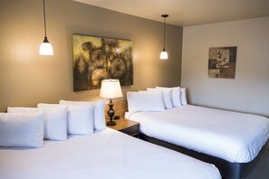 A hotel room with two beds, a nightstand with a lamp, and artwork on the walls.