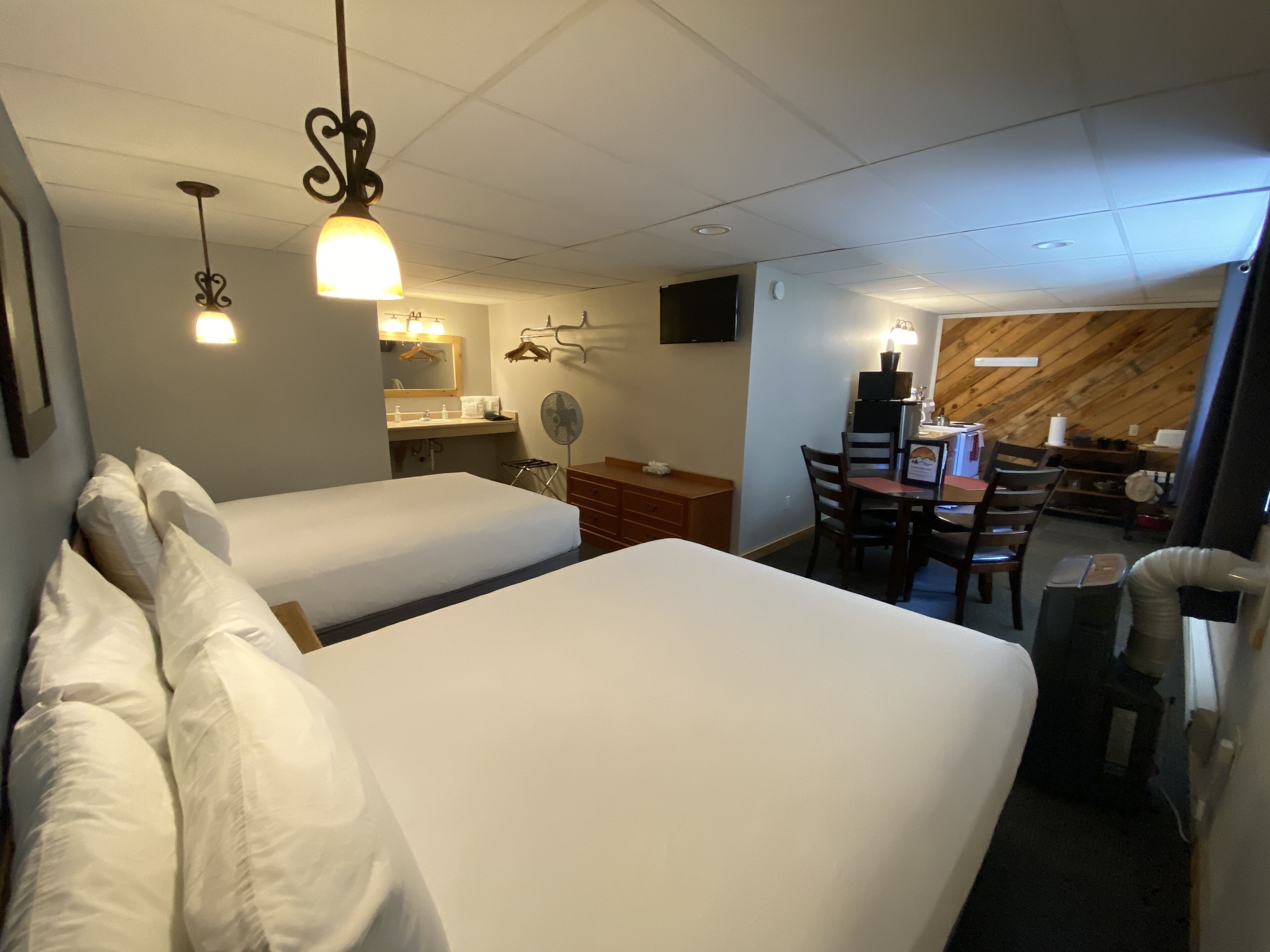A hotel room with two beds, a desk, a chair, a mirror, a television, and a wooden wall.