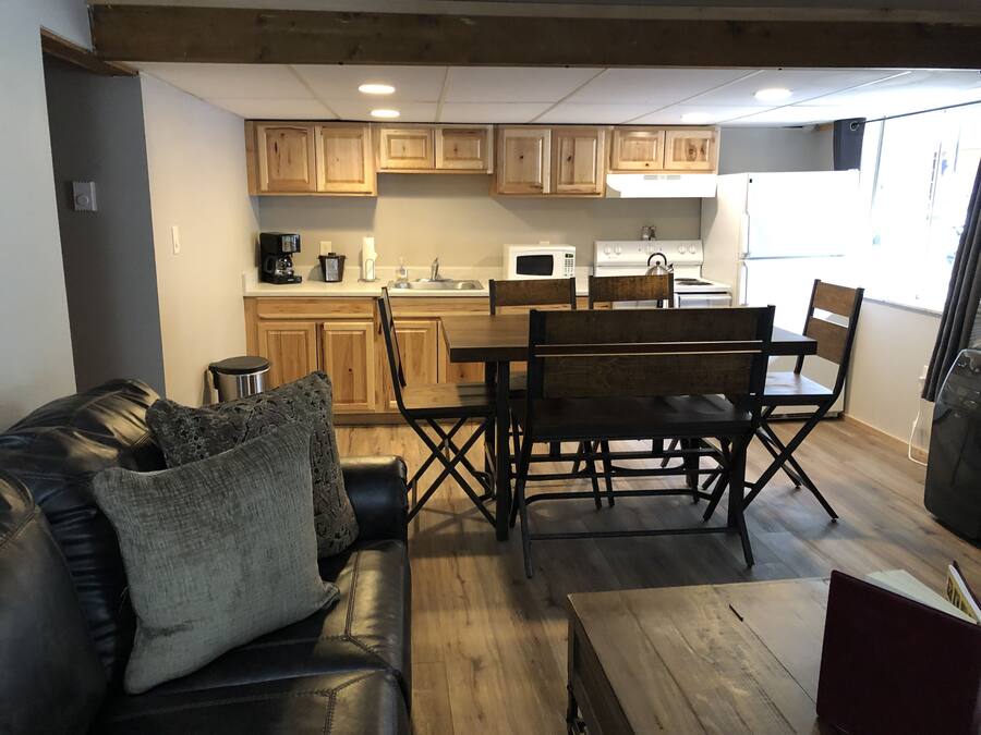 A compact living space with a kitchenette, wooden cabinets, a dining table with chairs, a leather sofa, and a small wooden coffee table.