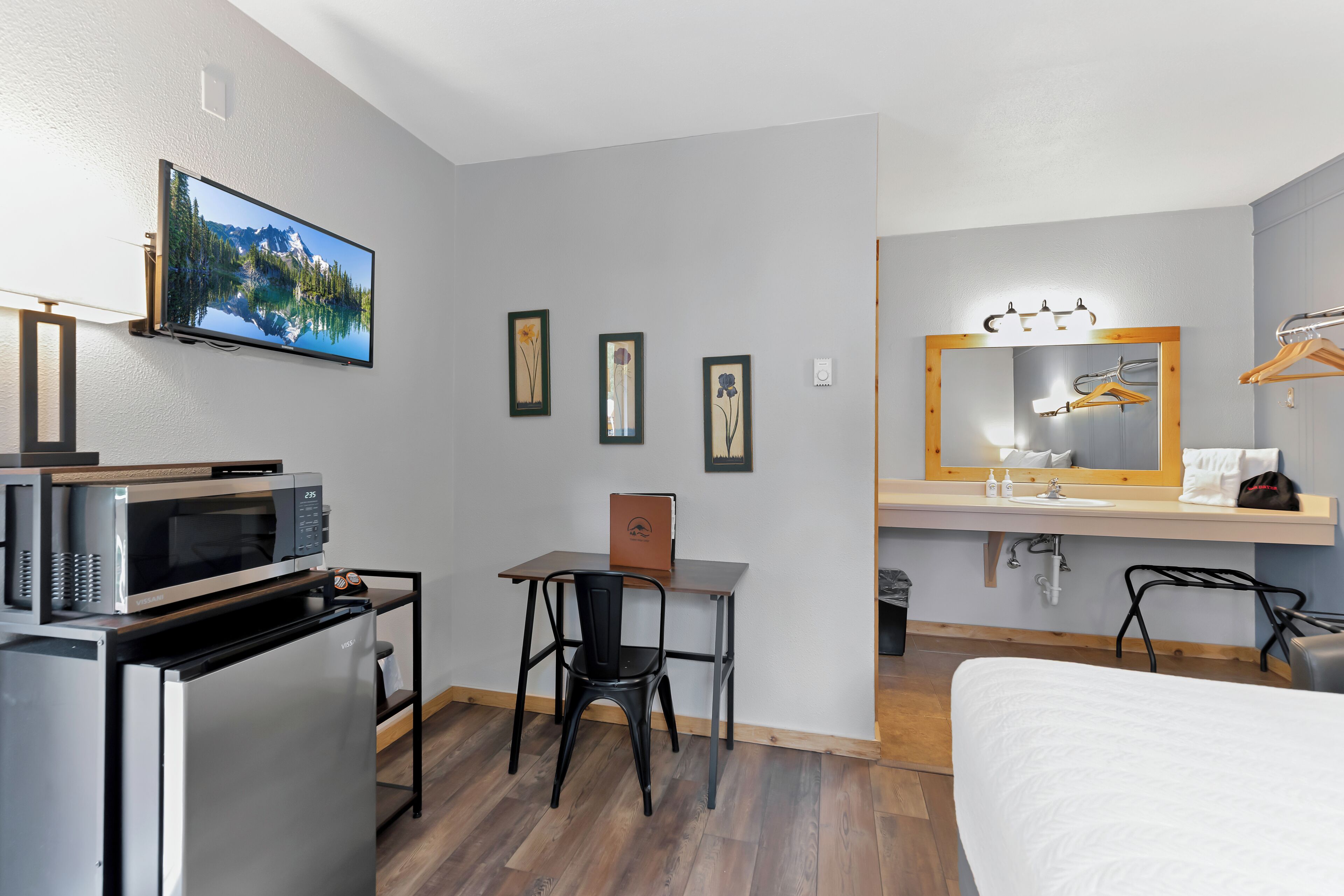Hotelkamer met een bed, een bureau met stoel, een magnetron, een koelkast, een televisie, een spiegel en een raam met uitzicht op de bergen.