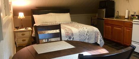 Ein gemütliches Schlafzimmer mit Bett, Nachttisch, Lampe und einer kleinen Küchenzeile.