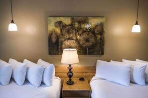 Habitación de hotel con dos camas, una mesita de noche de madera, una lámpara y un cuadro en la pared.