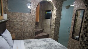 A bedroom with a stone wall, a bed with a grey bedspread, a wooden door, and a mirror on the wall. - Hotel 1973 (San Luis Potosi)