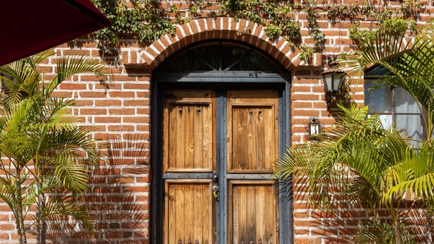 Un edificio de ladrillo con una puerta de madera doble y un pequeño ventanal arriba.