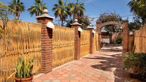 Un camino que lleva a una entrada portonada con muro de ladrillo y valla de bambú.