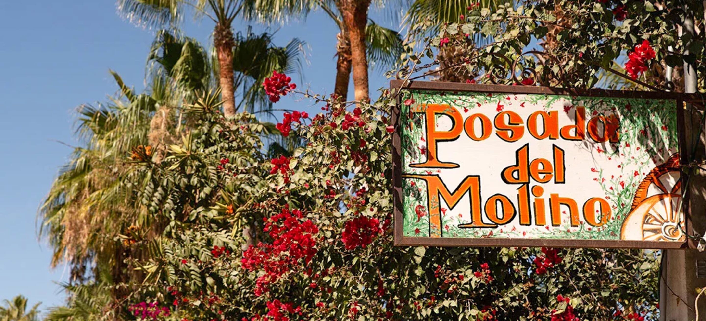 A sign with the text "Posada del Molino" surrounded by lush greenery and red flowers.