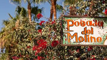 A sign with the text "Posada del Molino" surrounded by lush greenery and red flowers.