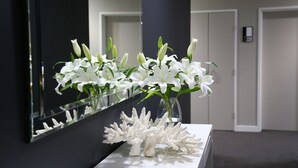A white vase with white flowers on a white table in a room with a dark wall and a mirror reflecting the flowers. - Springfield Lakes Boutique Hotel (Springfield Lakes)