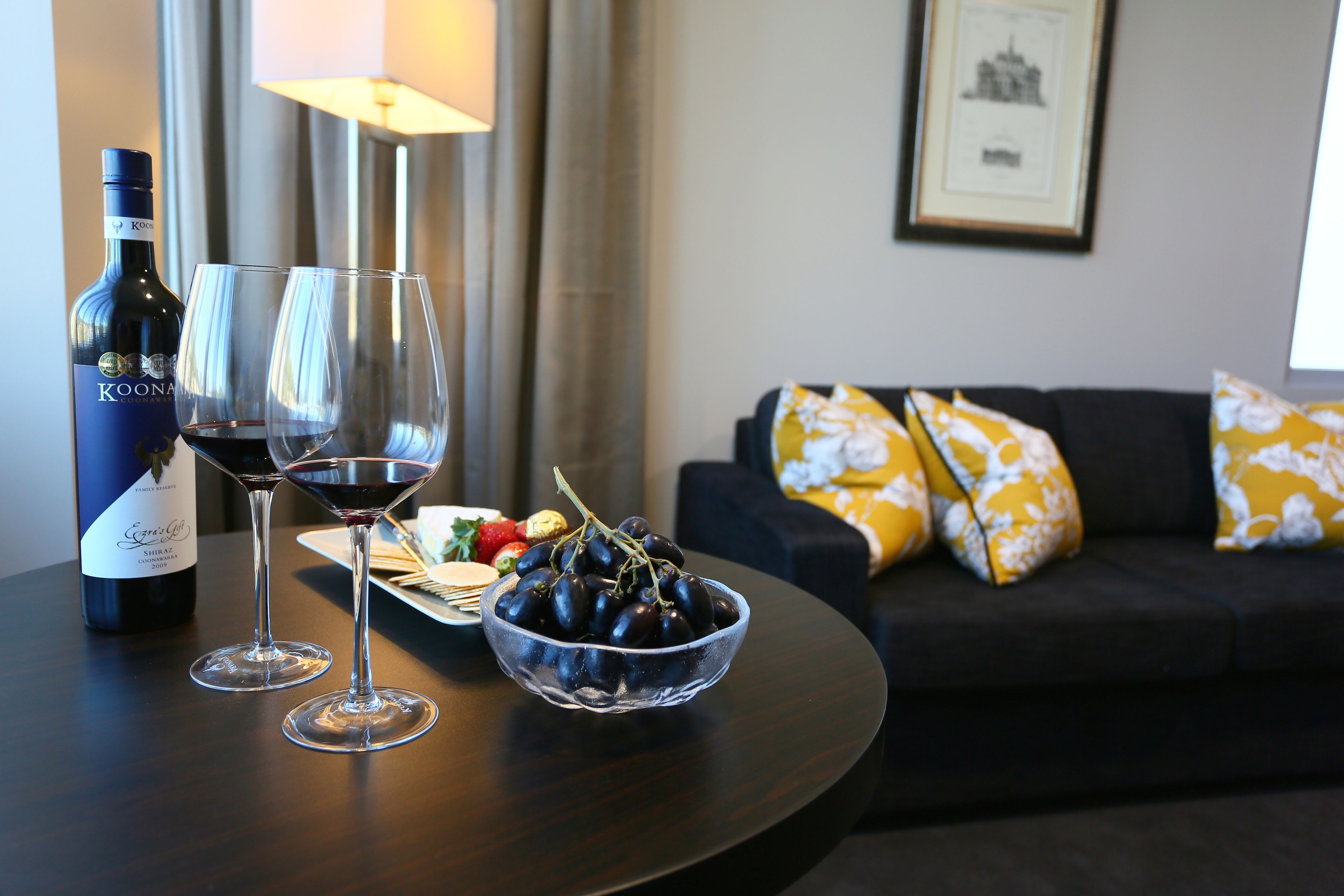 Una mesa de comedor con una botella de vino, dos copas de vino y un cuenco de uvas.