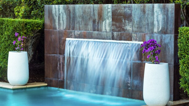 A pool with a waterfall feature and two large planters with purple flowers. - Springfield Lakes Boutique Hotel (Springfield Lakes)